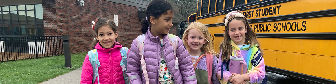 Group of four happy girls in front of a school bus